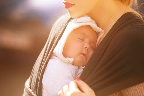 baby girl with eyes closed sleeping on her mother in sunny day.